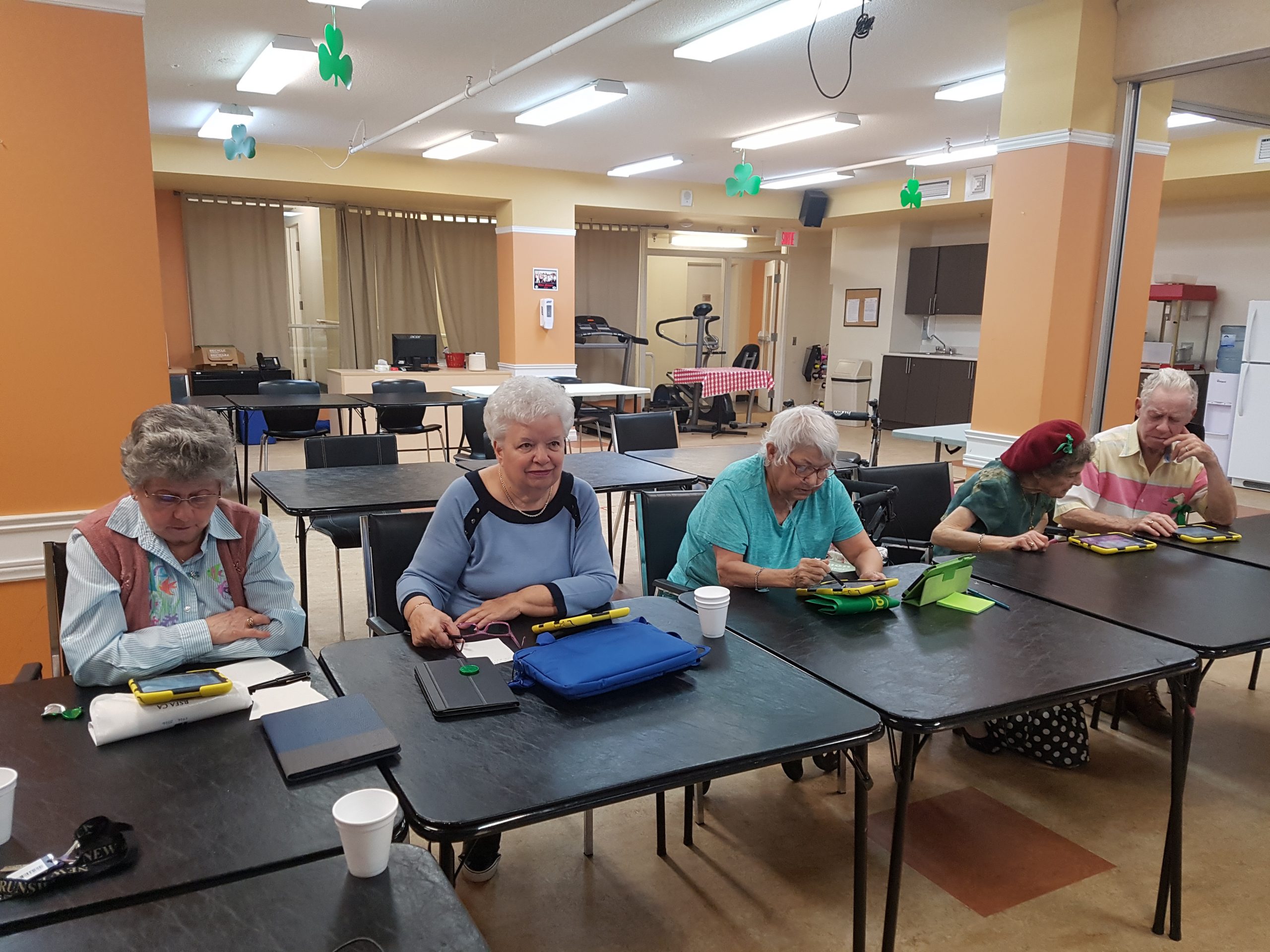 AlphaNumerique : Photo de personnes aînées assises à des tables avec des tablettes numériques